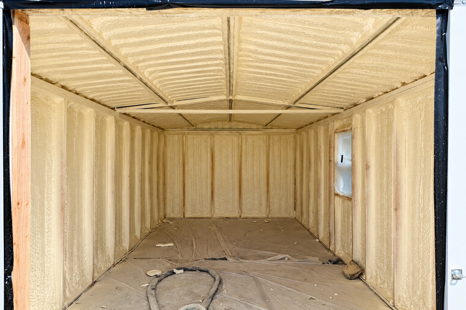 A small framed structure is coated inside with pale yellow closed-cell spray foam across its walls and ceiling.
