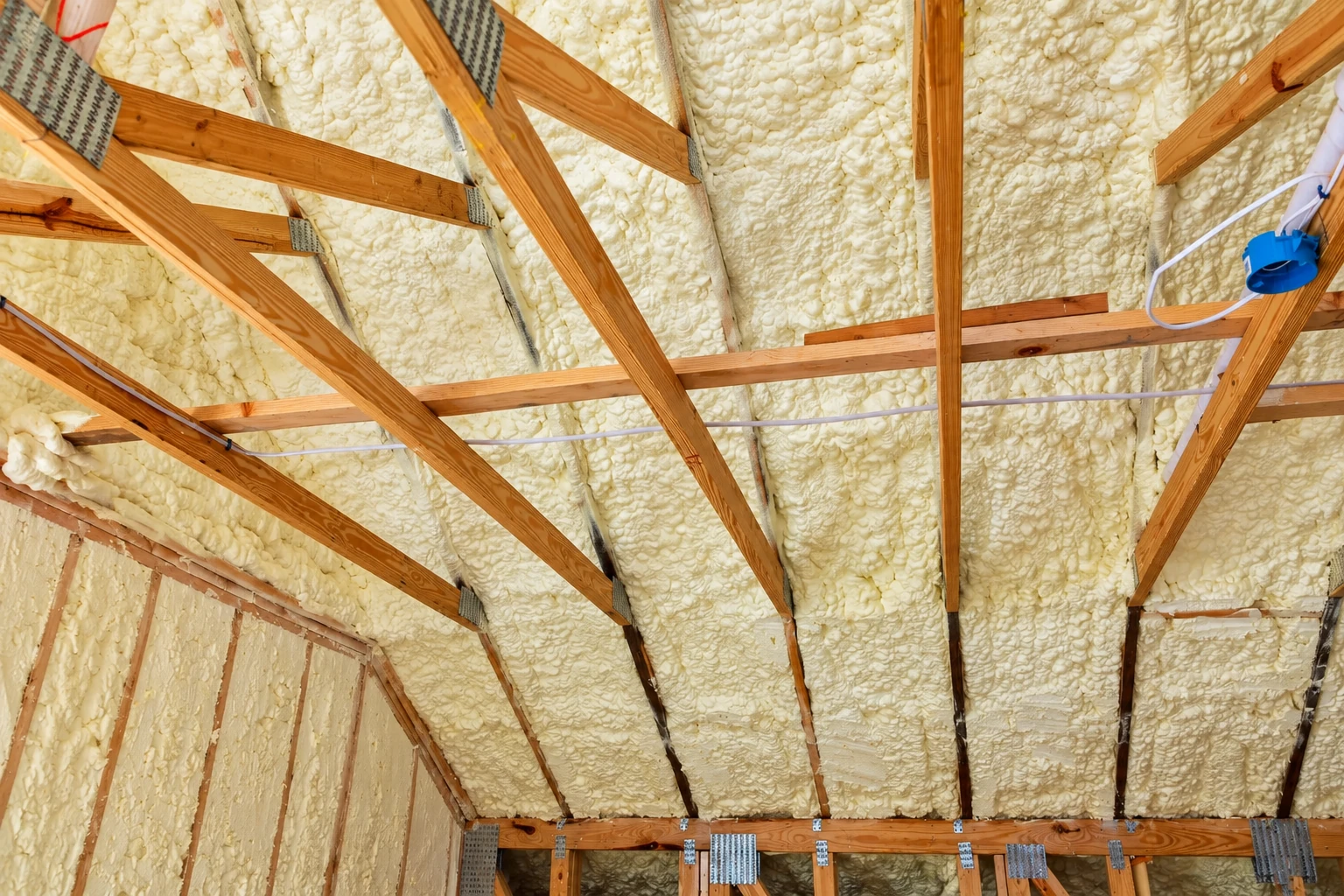 Spray foam insulation coats the underside of a home's roof between exposed wooden rafters.