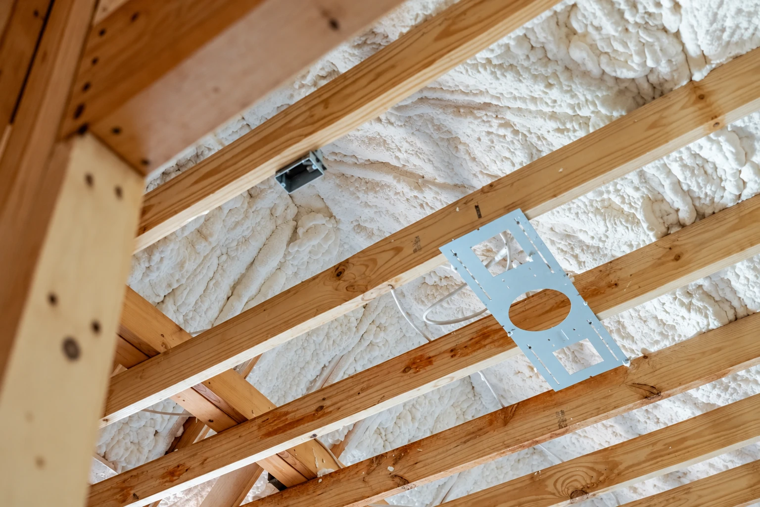 White spray foam insulation fills the spaces between exposed wooden roof trusses.